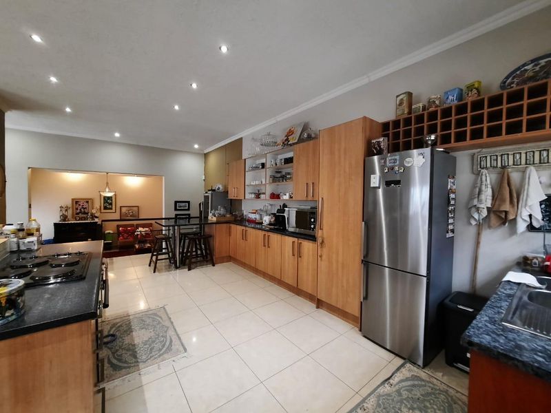 Spacious kitchen featuring light wood cabinetry, granite countertops, a gas hob, and integrated wine storage, flowing into an adjacent living area.
