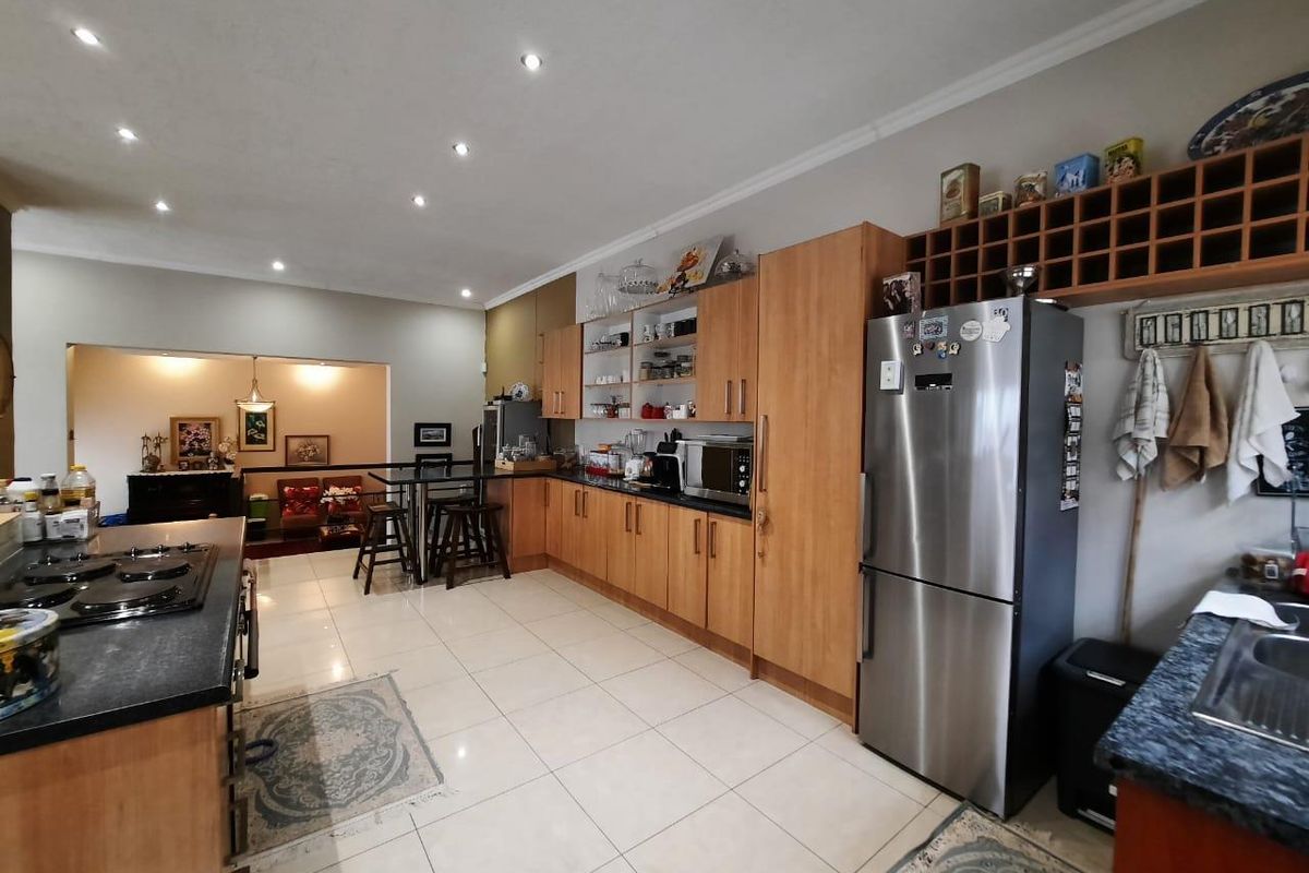 Spacious kitchen featuring light wood cabinetry, granite countertops, a gas hob, and integrated wine storage, flowing into an adjacent living area.