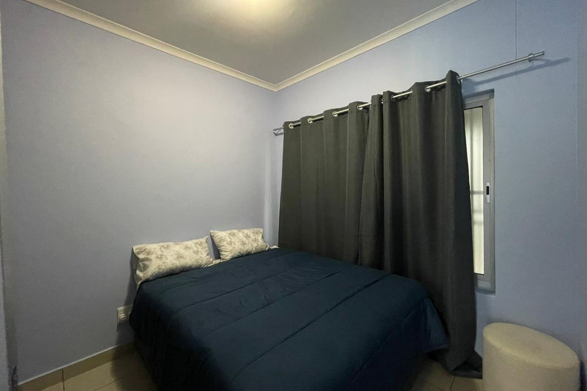 A compact bedroom featuring tiled flooring, light blue walls, and a window with curtain track.