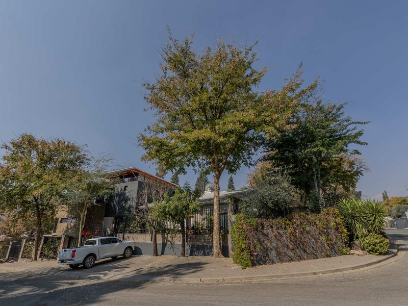 Street view of the property featuring a stone masonry boundary wall, metal security fencing, and mature trees providing privacy to the front facade.