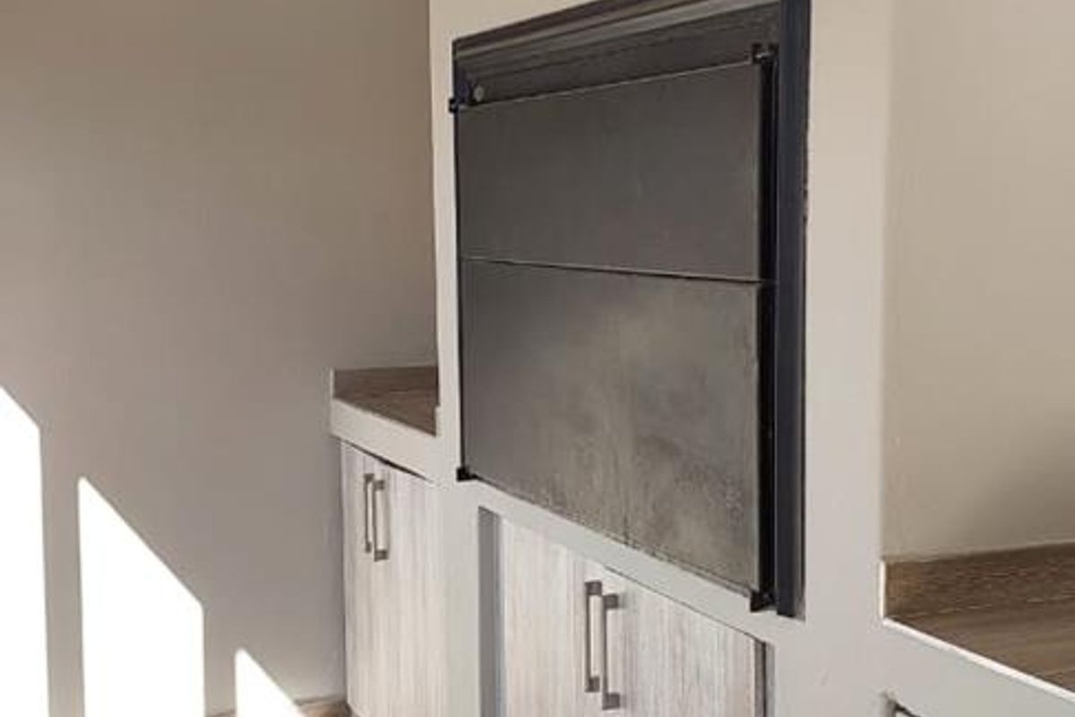 A clean indoor entertainment area featuring a built-in braai, wood-look tiled flooring, and modern cabinetry with ample storage space.