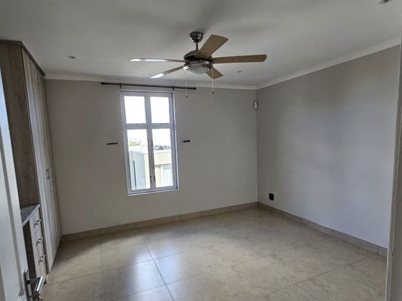 A spacious, empty bedroom featuring neutral tiled flooring, built-in cupboards, and a ceiling fan, offering a clean and versatile living space.