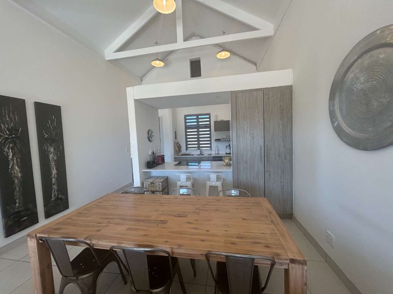 Open-plan living and dining area featuring a vaulted ceiling with exposed trusses, tiled flooring, and a modern kitchen with built-in cabinetry and island.