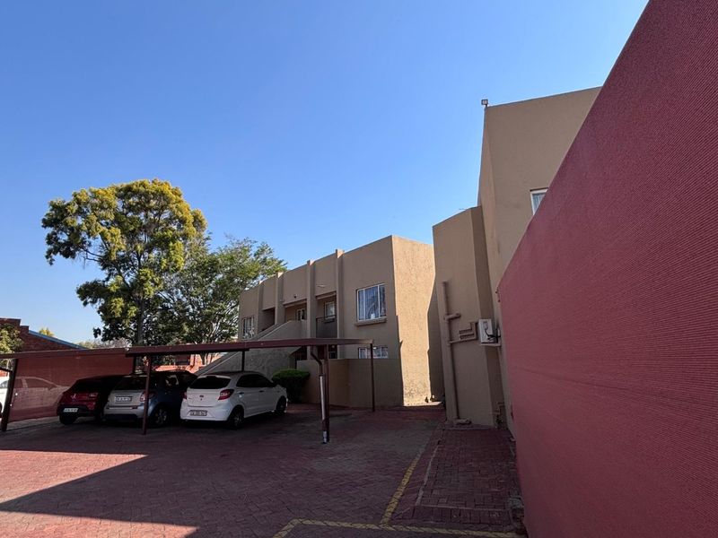 Exterior view of the apartment complex featuring a paved driveway, covered parking bays, and external building access via a staircase.
