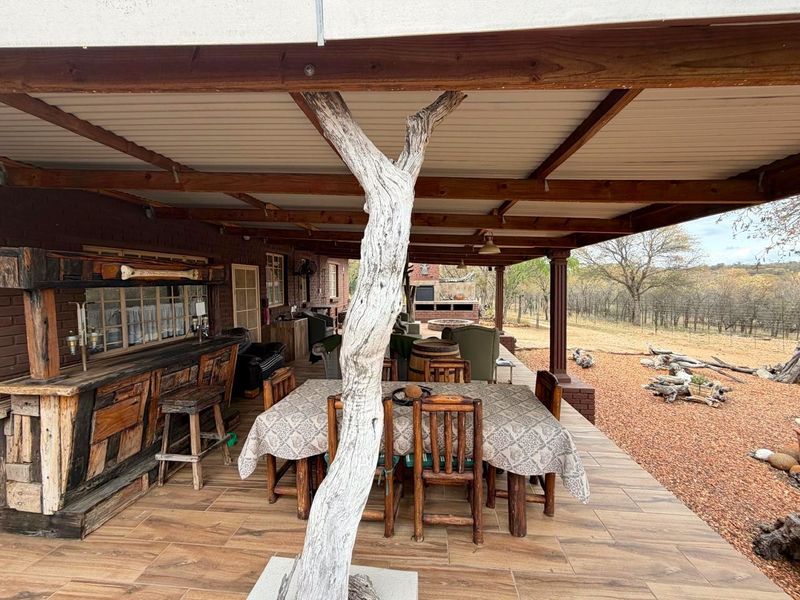 Spacious covered patio featuring a built-in bar and outdoor braai area, overlooking the natural landscape with durable tiled flooring and timber roof structure.