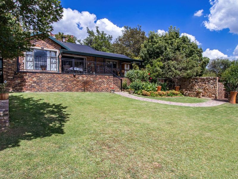 A well-maintained rear exterior view featuring a brick facade, a raised patio with wrought iron railings, and a spacious landscaped garden with paved pathways.