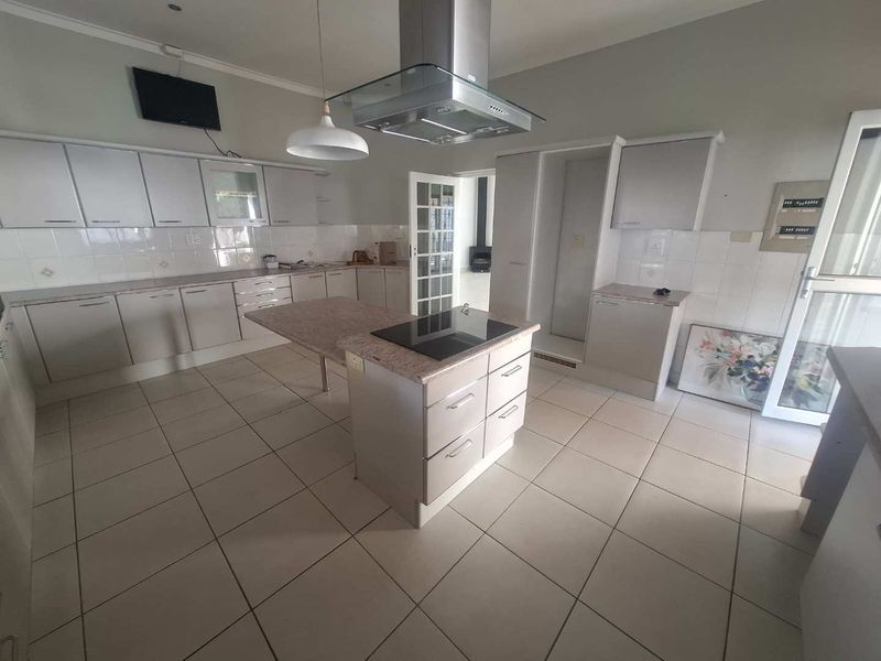 Spacious kitchen featuring a central island with integrated hob, overhead extractor fan, ample cabinetry, and tiled flooring throughout.