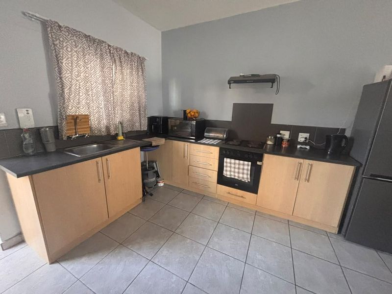 A functional kitchen featuring light wood-finish cabinetry, dark countertops, tiled backsplash, and built-in cooking appliances including an oven and extractor fan.
