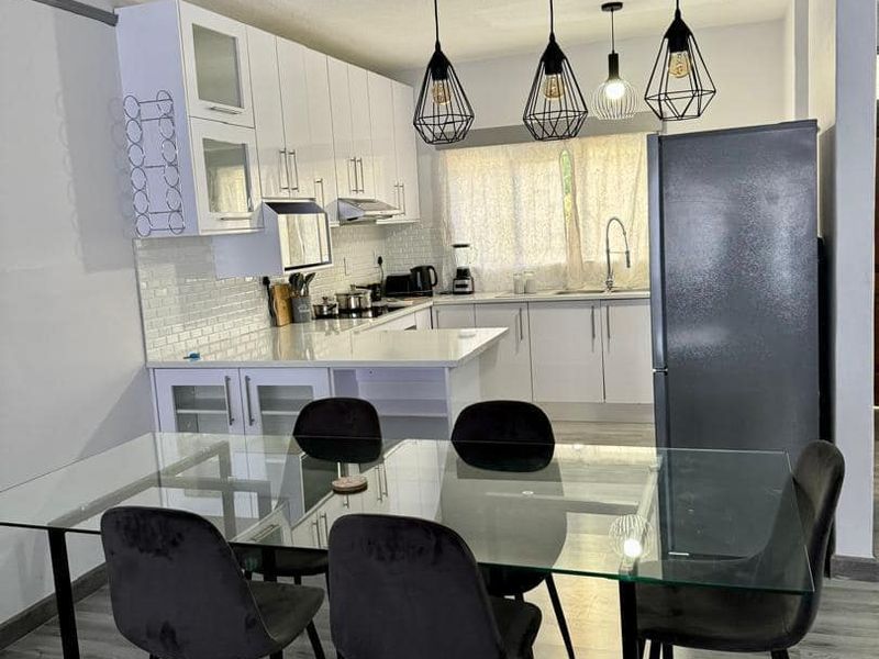 Modern open-plan kitchen and dining area featuring white cabinetry, subway tile backsplash, contemporary pendant lighting, and durable laminate flooring.