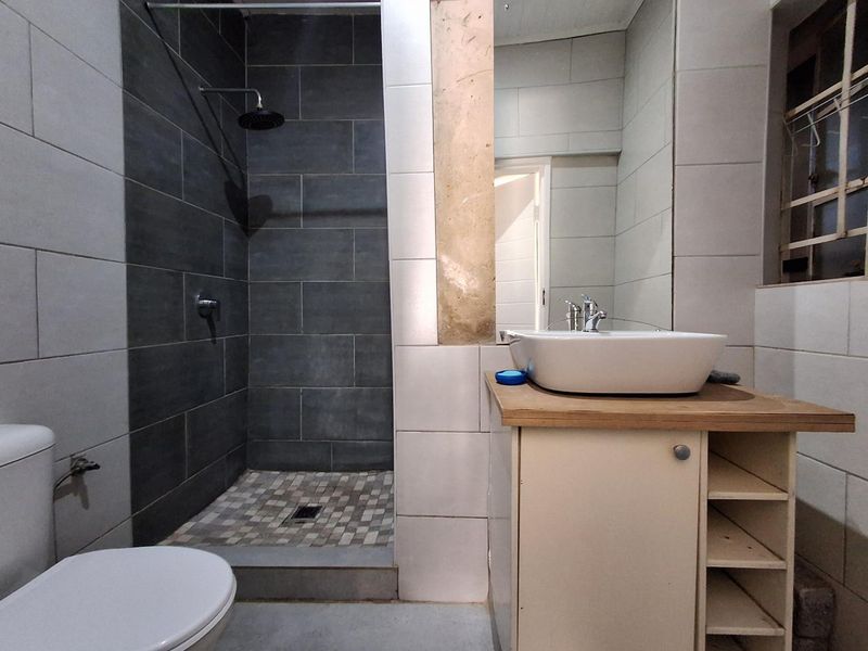 Modern bathroom featuring a walk-in shower with dark tiling, a vessel sink on a wooden vanity, and a large wall mirror.