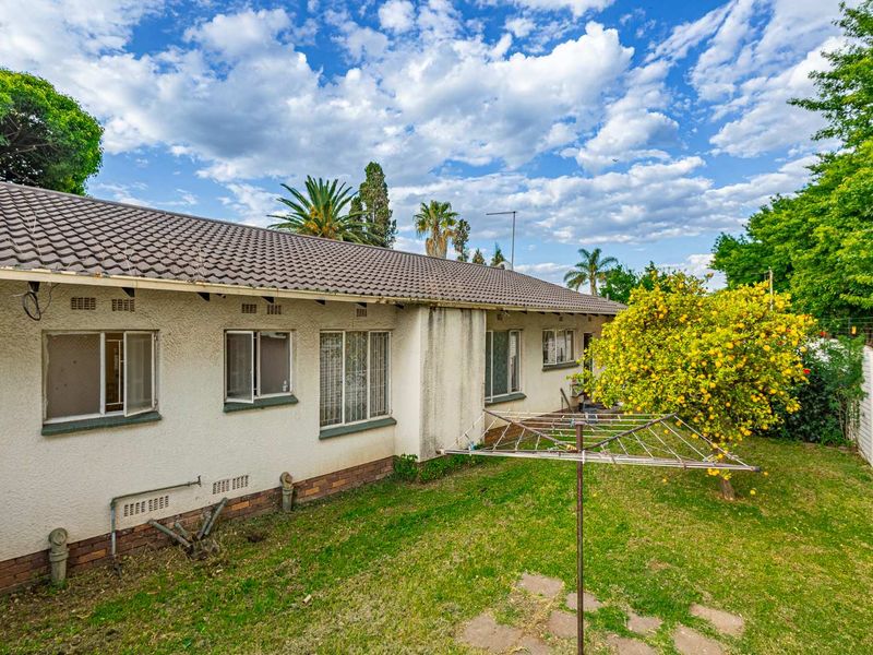 Rear view of the house featuring a tiled roof, plastered exterior walls with security bars, and a private garden area.