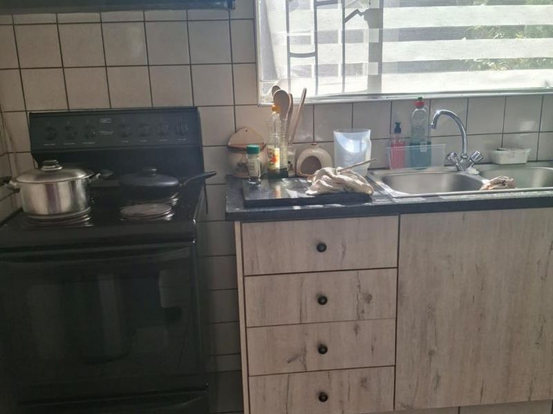 A functional kitchen featuring laminate cabinetry, a freestanding stove with extractor fan, double sink, and tiled backsplash.