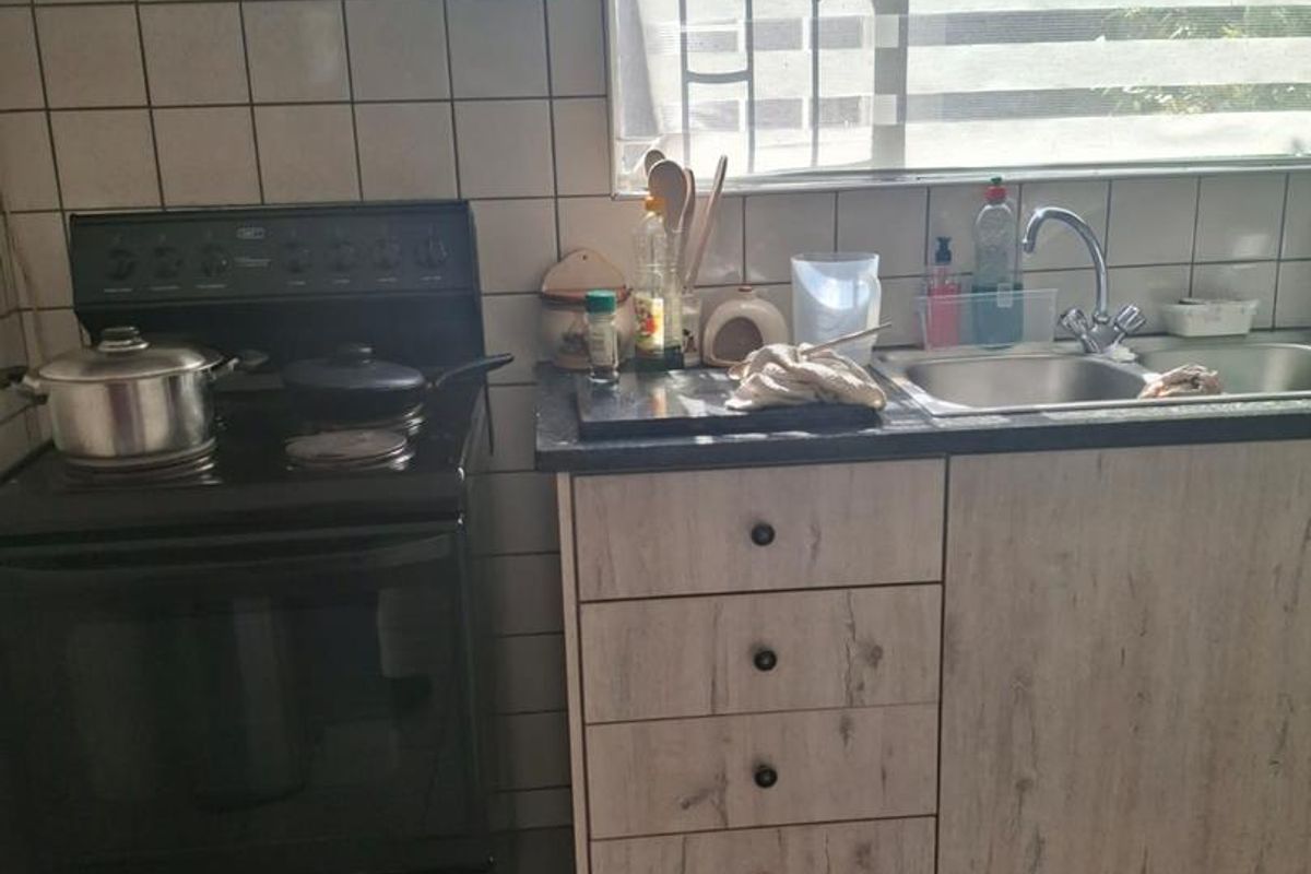 A functional kitchen featuring laminate cabinetry, a freestanding stove with extractor fan, double sink, and tiled backsplash.