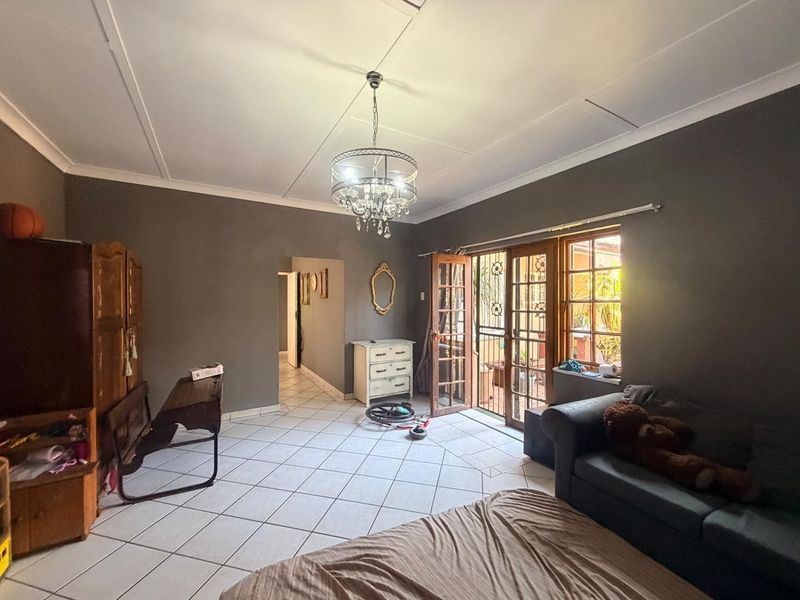 Spacious living room featuring tiled flooring, a decorative chandelier, and direct access to the patio through classic wooden french doors.