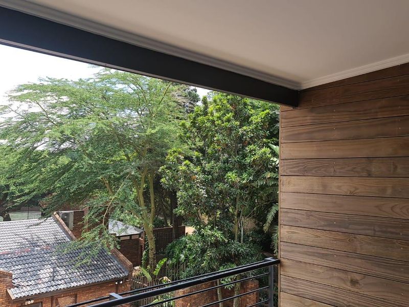 A covered balcony featuring timber wall cladding and a metal balustrade, offering a pleasant view of the surrounding trees and neighborhood.