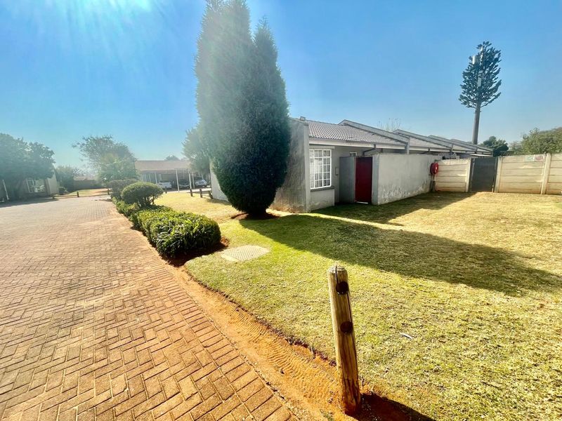 Front exterior view of the cluster property featuring a paved driveway, well-maintained lawn, and established garden area.