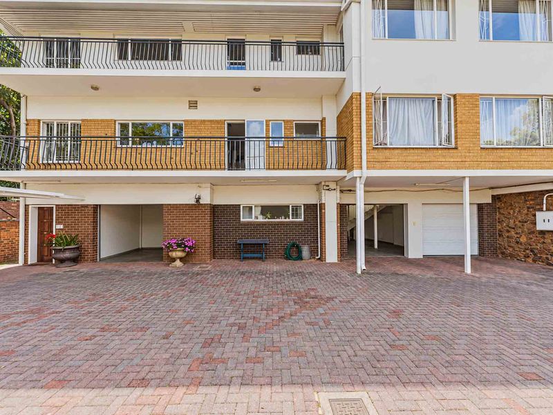 Front exterior view of a multi-level residential building featuring brick paving, integrated garage access, and upper-level balconies with metal railings.