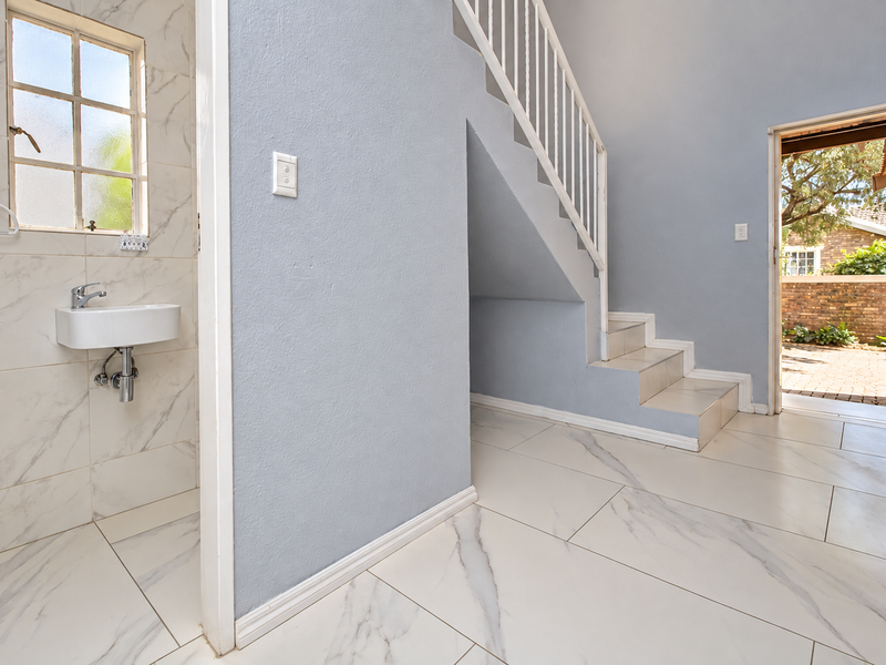 Bright entrance area featuring marble-look tiling, a wall-mounted basin, and a staircase leading to the upper level with direct access to the exterior.