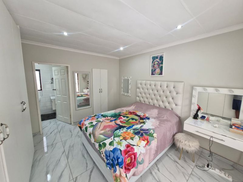 A well-maintained bedroom featuring modern marble-look floor tiles, recessed downlighting, built-in cabinetry, and direct access to an en-suite bathroom.