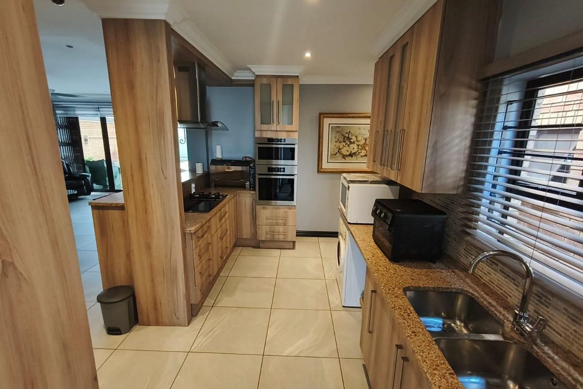 Modern kitchen featuring wood-finish cabinetry, granite countertops, integrated appliances, and tiled flooring, offering a functional and well-maintained workspace.
