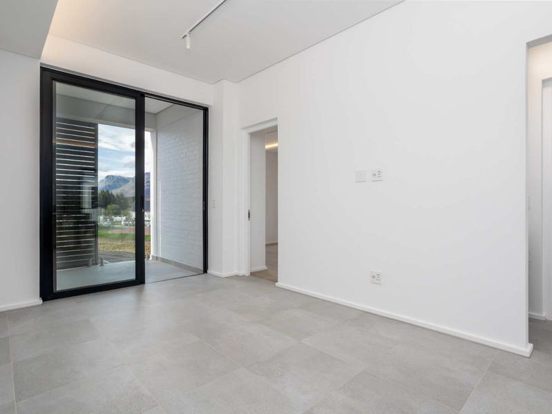 A bright, modern, empty bedroom featuring large sliding glass doors leading to a balcony, neutral tiled flooring, and clean white finishes.