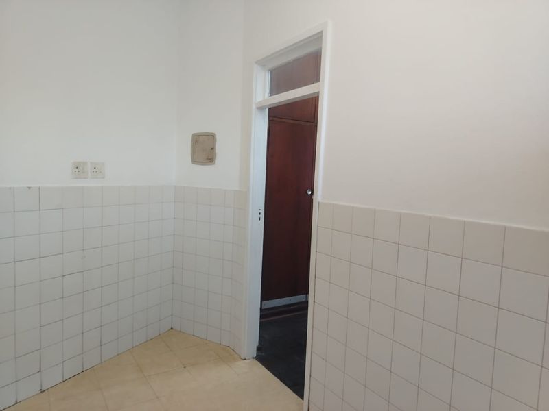 An empty kitchen area featuring white tiled splashbacks and neutral floor tiles, providing a blank canvas for renovation or modernization.