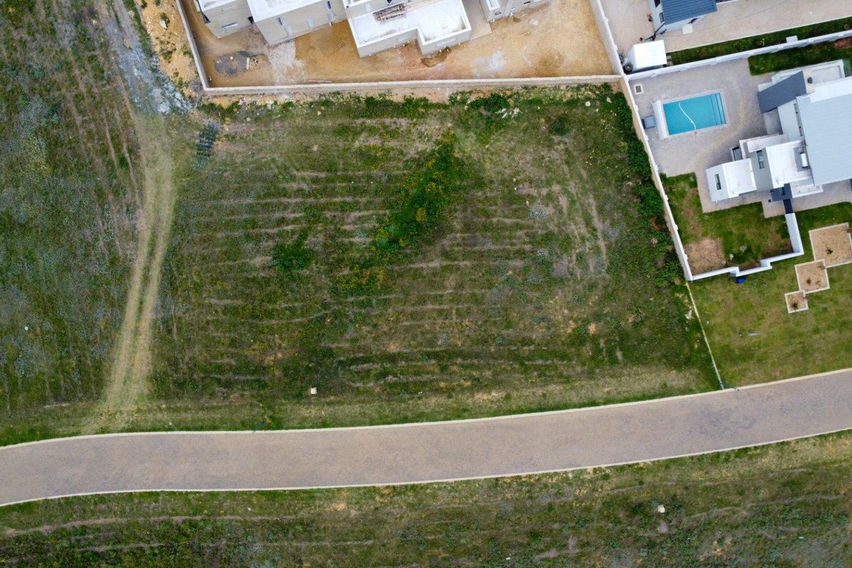 Aerial view of a vacant residential plot situated in a developed estate, featuring direct road access and established surrounding properties.