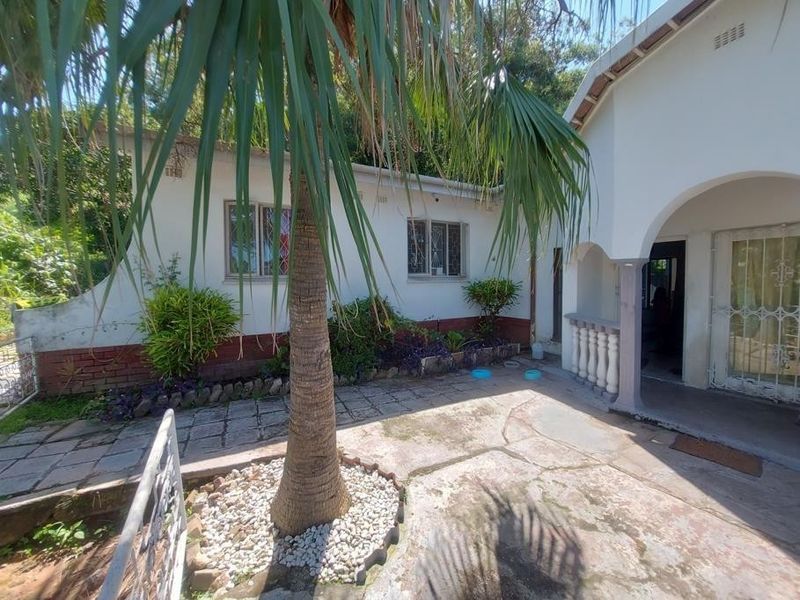Front entrance area featuring a covered patio, concrete paving, and security gate access to the main residence.
