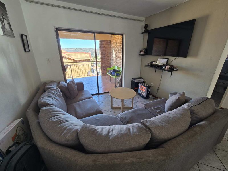 A living room featuring tiled flooring and a sliding glass door that opens onto a balcony with views.