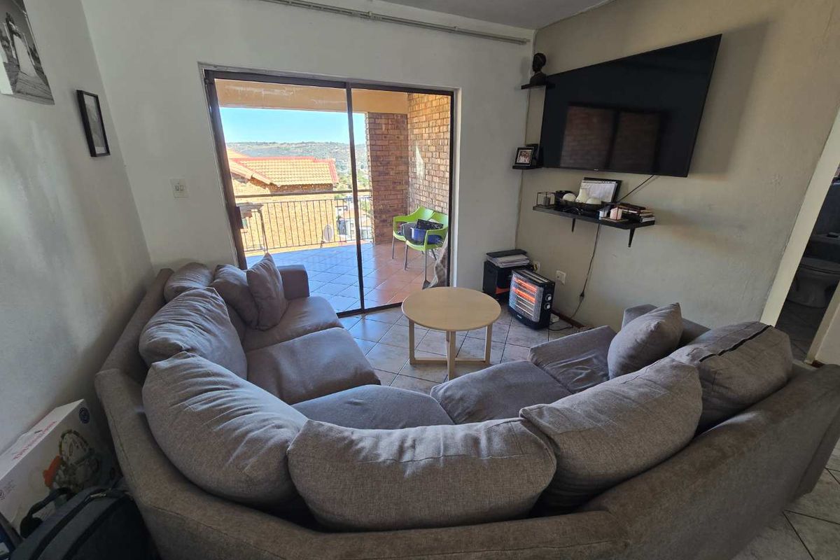 A living room featuring tiled flooring and a sliding glass door that opens onto a balcony with views.