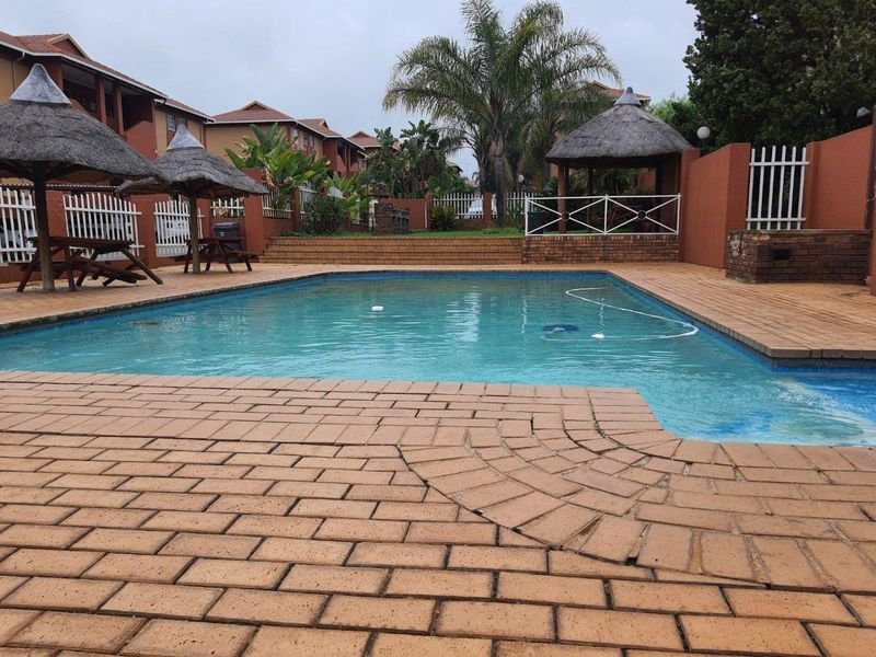 Communal swimming pool area featuring brick paving, a built-in braai, and a thatched lapa within a secure apartment complex setting.