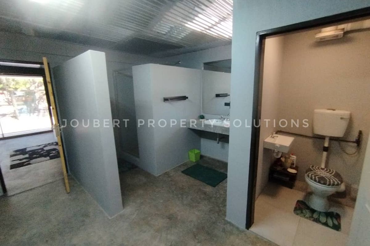 A functional bathroom area featuring a separate toilet cubicle, open shower space, and wall-mounted basin with exposed industrial-style finishes.