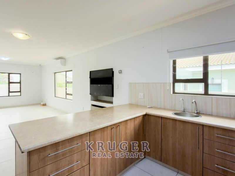 Spacious open-plan living area featuring a modern kitchen with wood-finish cabinetry, laminate countertops, and a built-in fireplace, finished with neutral tiled flooring.