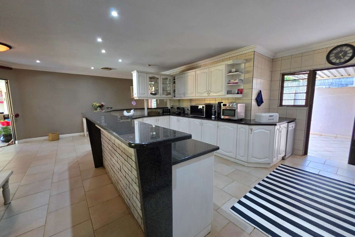 Spacious kitchen featuring a large granite-topped breakfast bar, white cabinetry, tiled flooring, and recessed ceiling lighting, offering a functional open-plan layout.