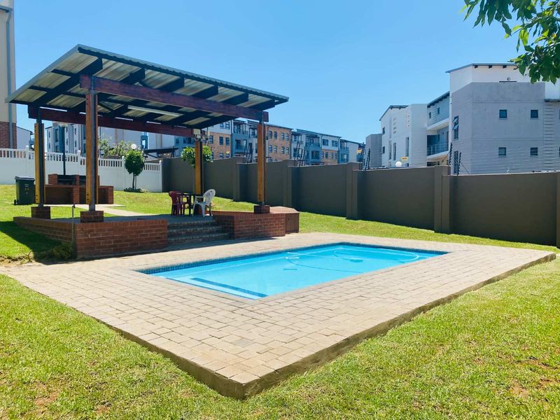 Outdoor pool area featuring a paved deck, a covered patio structure with a built-in brick braai, and secure perimeter walling.