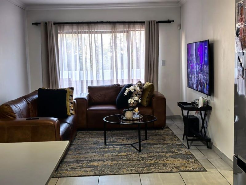 A comfortable living room featuring tiled flooring and a large window with curtain treatments, providing a functional and well-lit space.