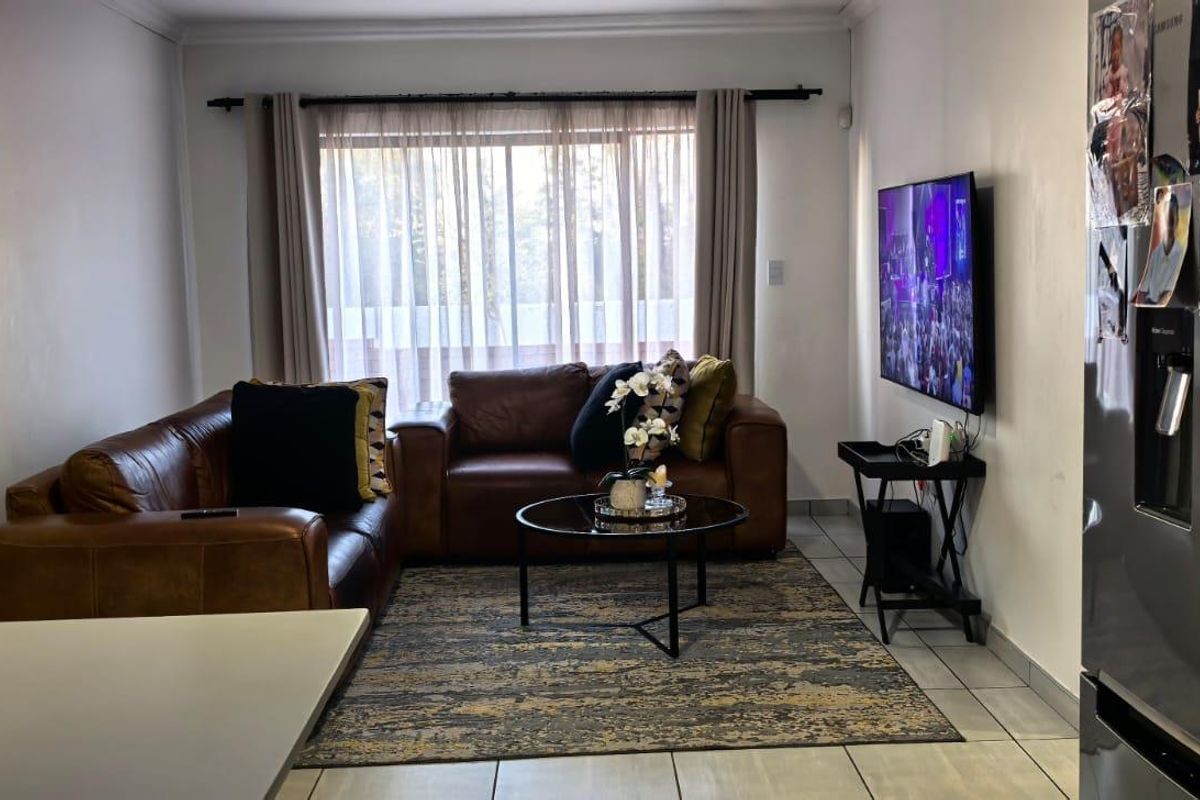 A comfortable living room featuring tiled flooring and a large window with curtain treatments, providing a functional and well-lit space.