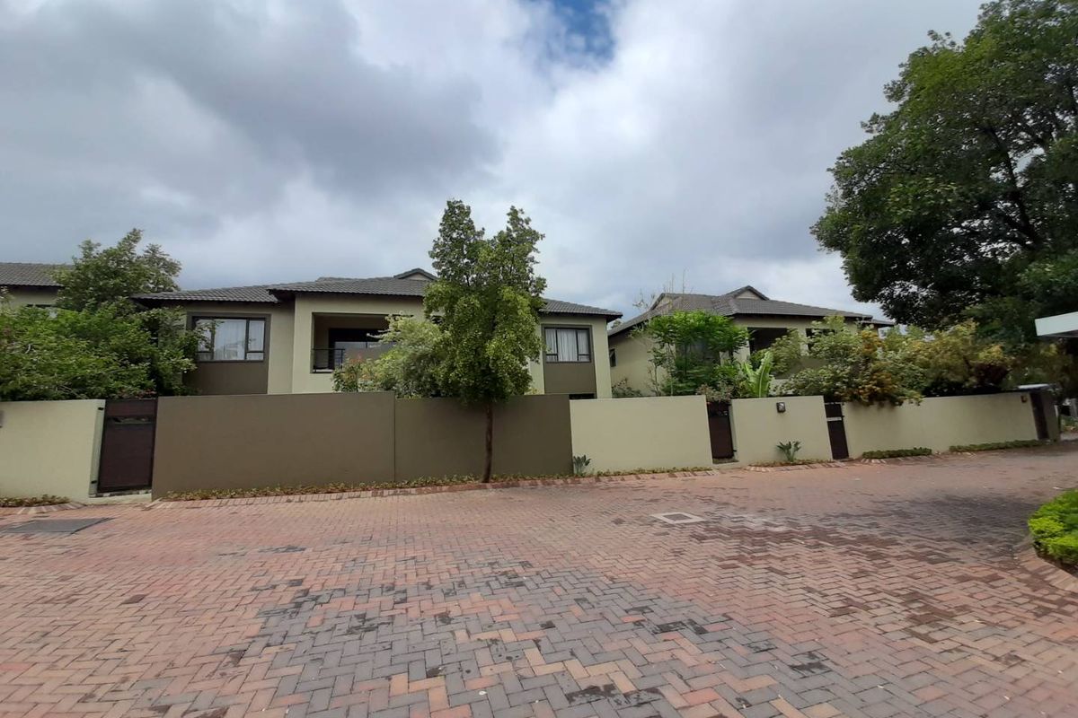 Street view of the apartment complex featuring a paved driveway, perimeter wall, and well-maintained building facades with tiled roofing.