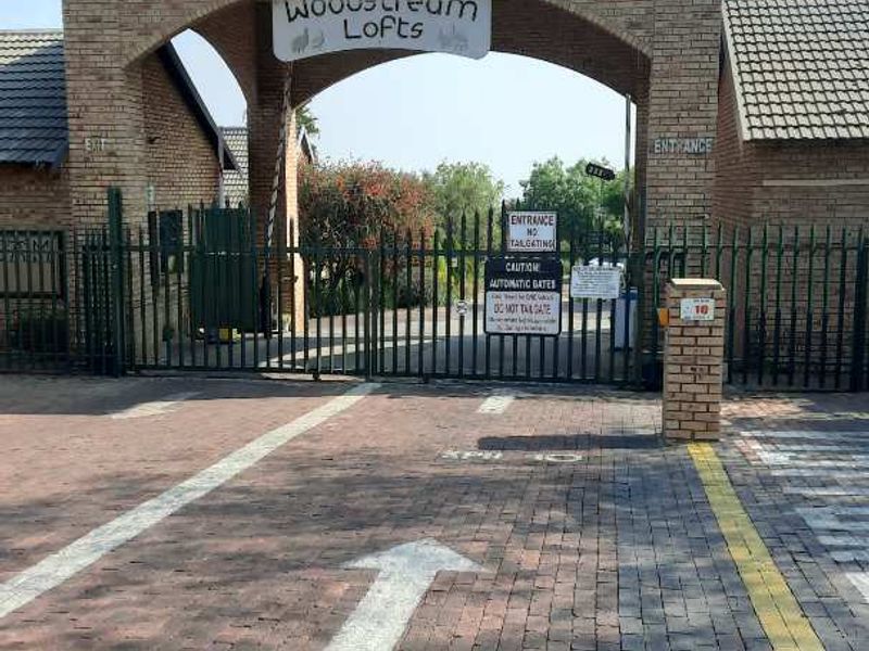 The main entrance gate to Woodstream Lofts, featuring a brick archway, security fencing, and paved driveway access.