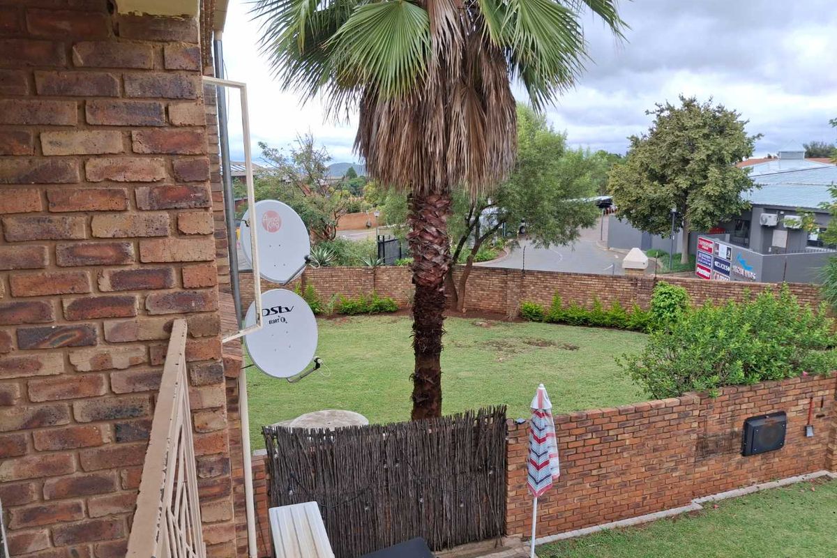An elevated view overlooking a private garden area with brick boundary walls, established palm tree, and residential street access.