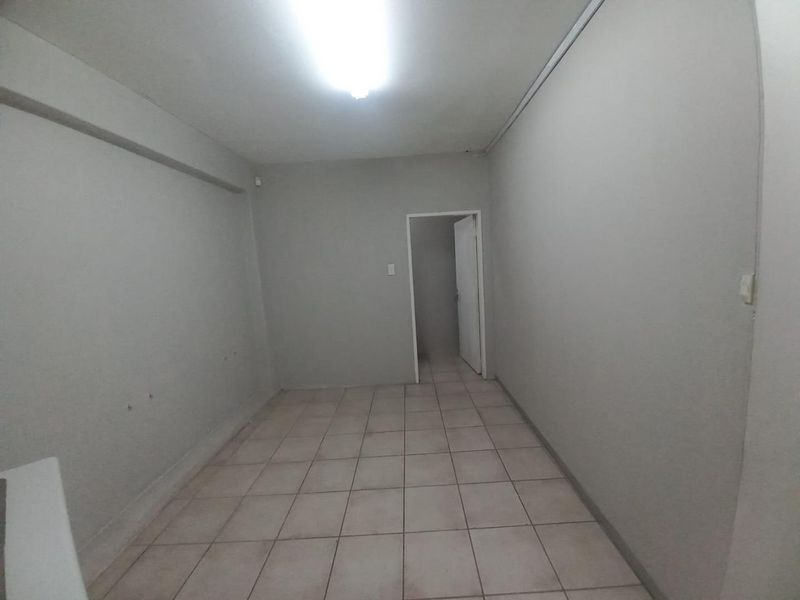 An empty, neutral-toned office space featuring tiled flooring and overhead lighting, suitable for a variety of business configurations.