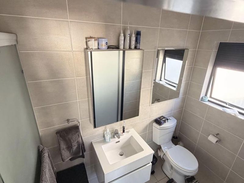 A modern, well-maintained bathroom featuring a wall-mounted vanity, integrated basin, mirror cabinet, toilet, and a glass-enclosed shower with neutral wall and floor tiling.