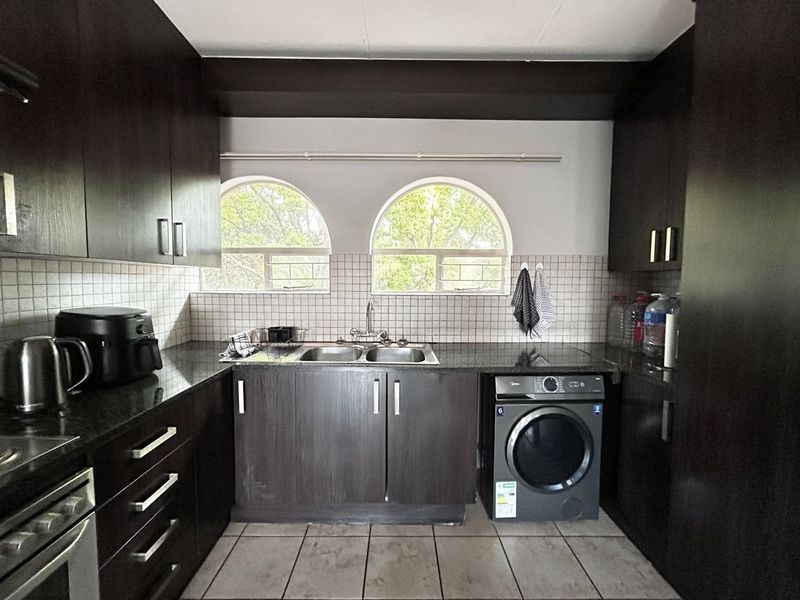 A functional kitchen featuring dark wood cabinetry, granite countertops, a double basin sink, and arched windows, providing a practical and well-organized workspace.