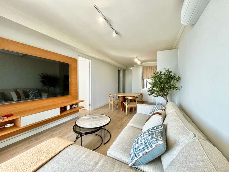 Modern open-plan living and dining area featuring light wood-look flooring, a custom built-in media wall, and efficient split-system air conditioning.