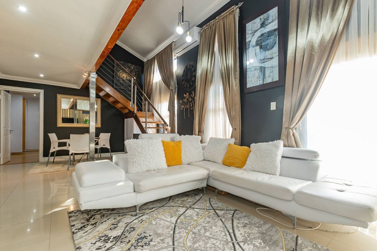 Spacious living room featuring high ceilings, a modern staircase with metal balustrades, tiled flooring, and split-system air conditioning.