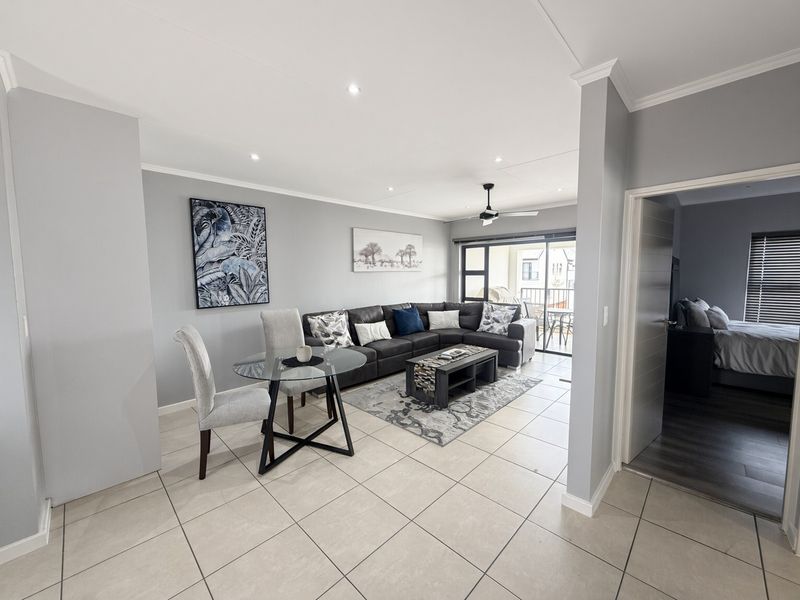 A bright open-plan living and dining area featuring neutral tiled flooring, recessed lighting, and a sliding glass door leading to an outdoor balcony.