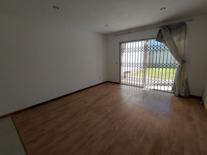 An empty living room featuring laminate flooring, recessed downlights, and a sliding glass door with a security gate leading to the exterior.