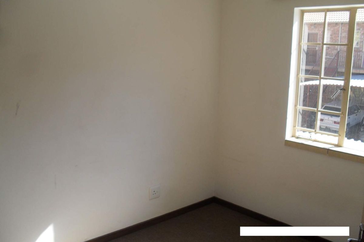 An empty bedroom featuring a window with security bars, neutral walls, and carpeted flooring, ready for personalization.