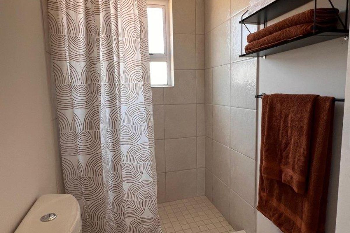 A functional bathroom featuring a shower with a curtain, a toilet, and neutral wall and floor tiling.