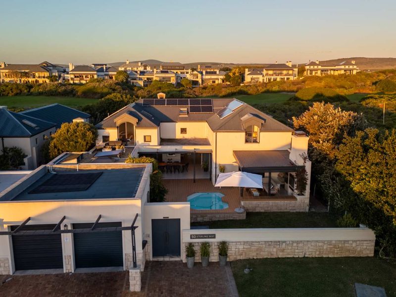Aerial view of a modern residential property featuring a swimming pool, covered patio, solar panels, and a double garage in a landscaped estate setting.